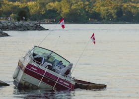 A motorboat partially submerged near the shore, displaying Canadian flags.